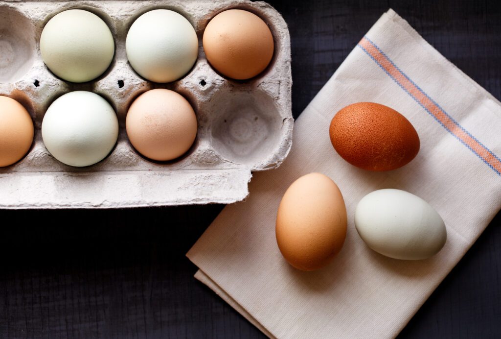 A carton of duck and chicken eggs on a counter with three eggs on a napkin next to it.